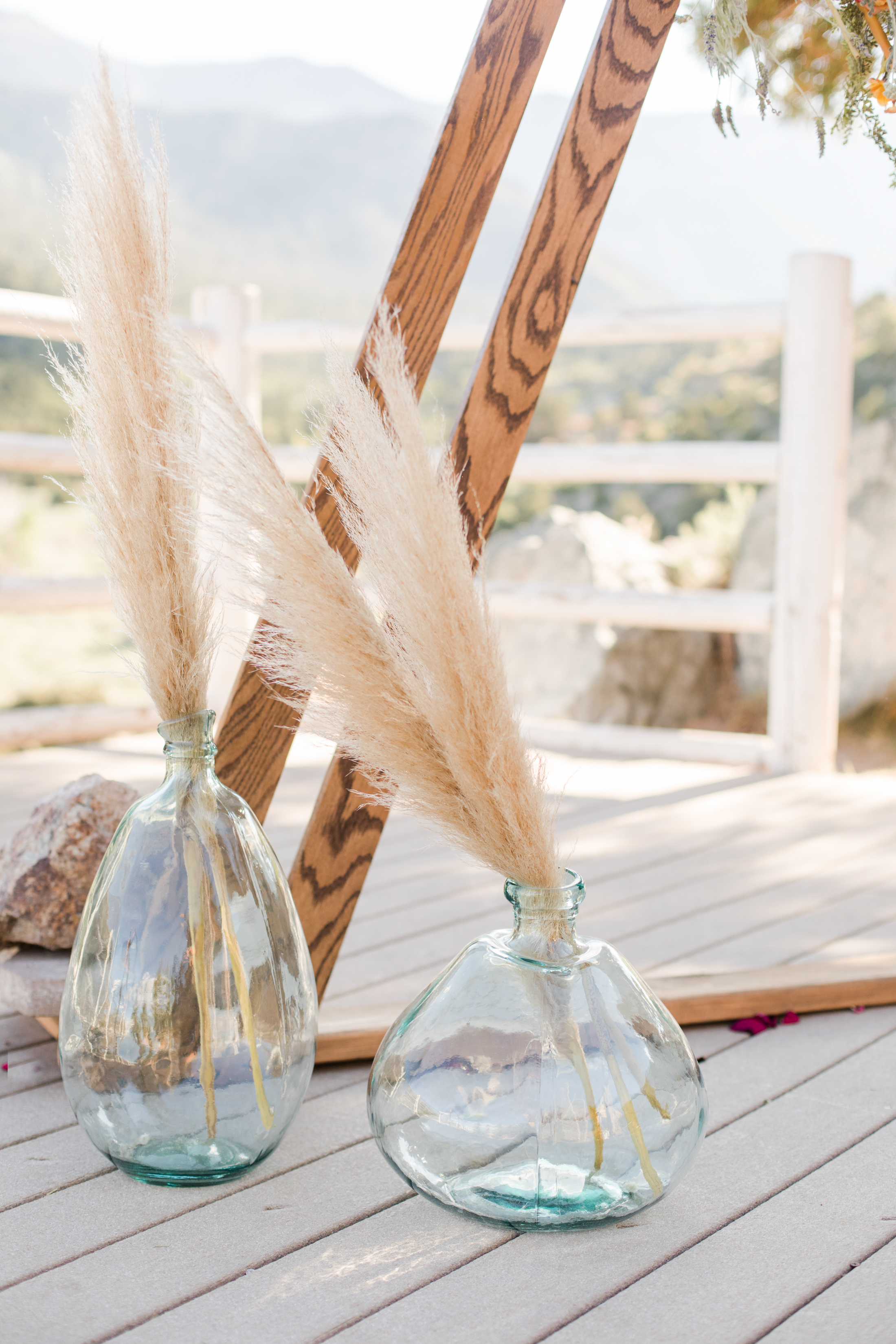 Pampas grass in glass vases beside a wooden arch