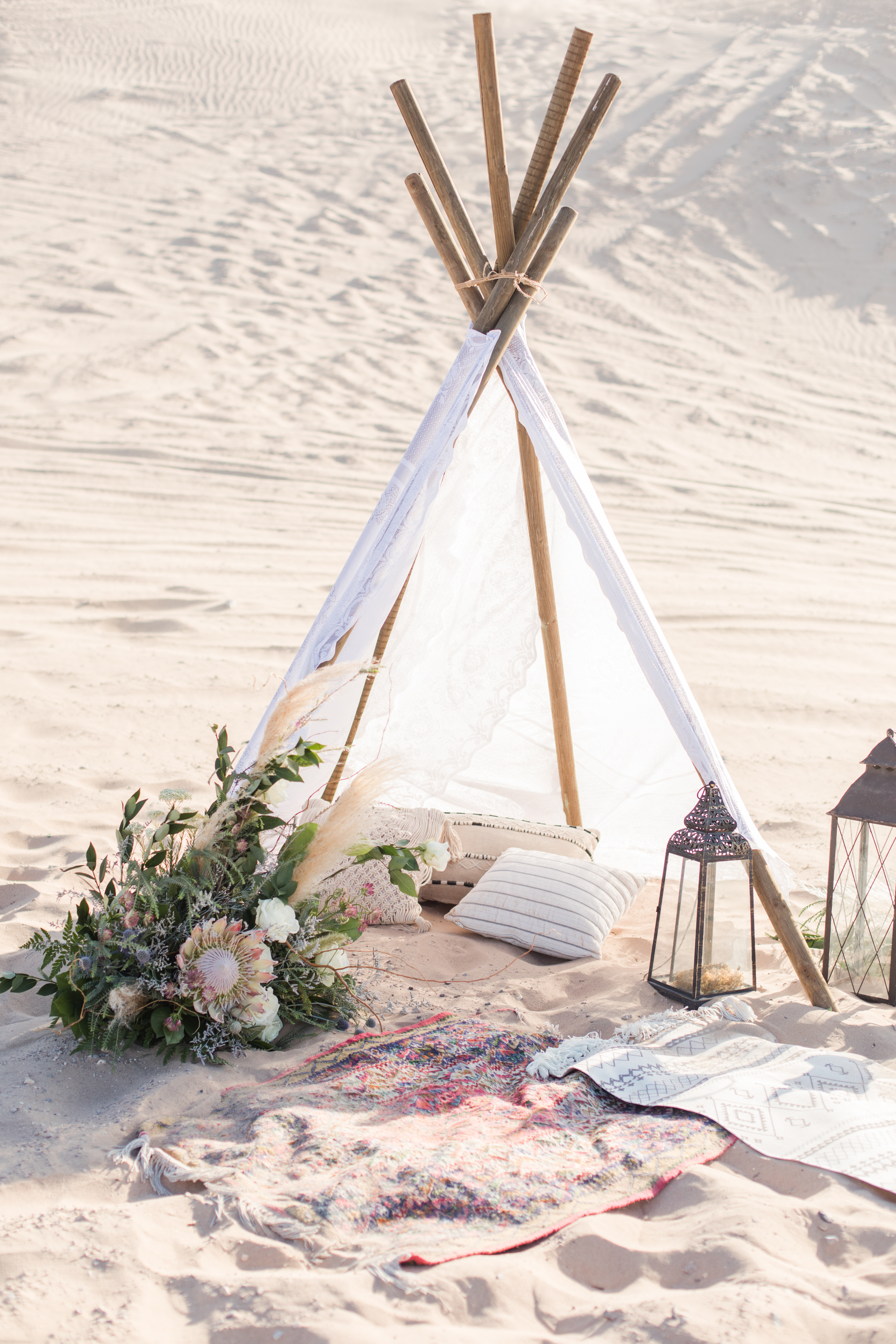 A lace teepee with cushions and lanterns set up on sand dunes